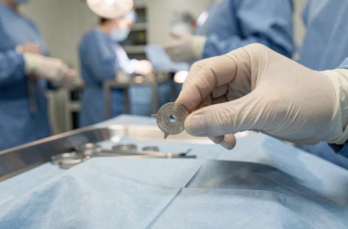 Gros plan de mains gantées tenant un stent coronarien métallique en salle d'opération, illustrant les risques post-opératoires